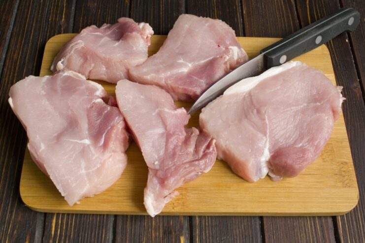 Cut pork into thick, uniform slices for even cooking A piece of raw pork being sliced into thick steaks on a cutting board.