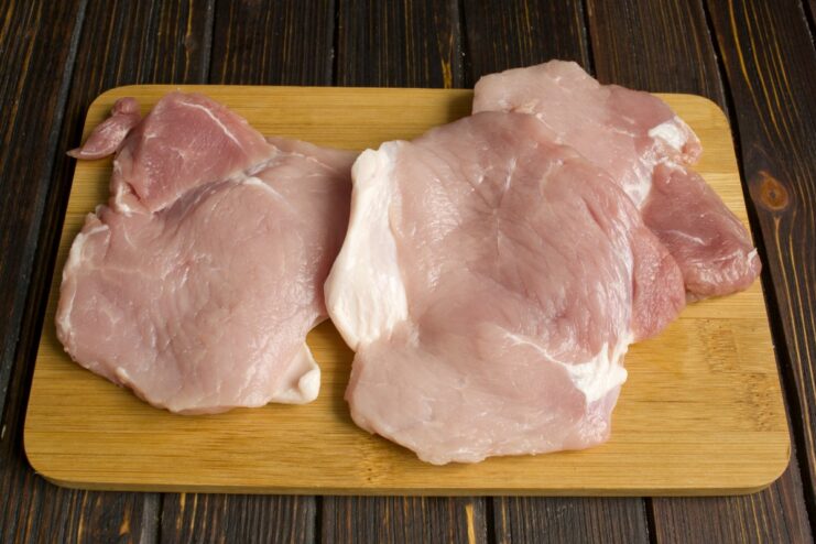 Tenderizing the pork helps to make it extra juicy and soft after baking Slices of pork being tenderized with a meat mallet.
