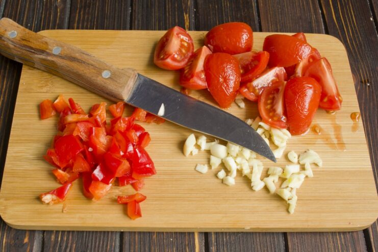 Preparing a fresh vegetable sauce with tomatoes, garlic, and bell peppers Chopped garlic, tomatoes, and bell peppers on a cutting board for the sauce.
