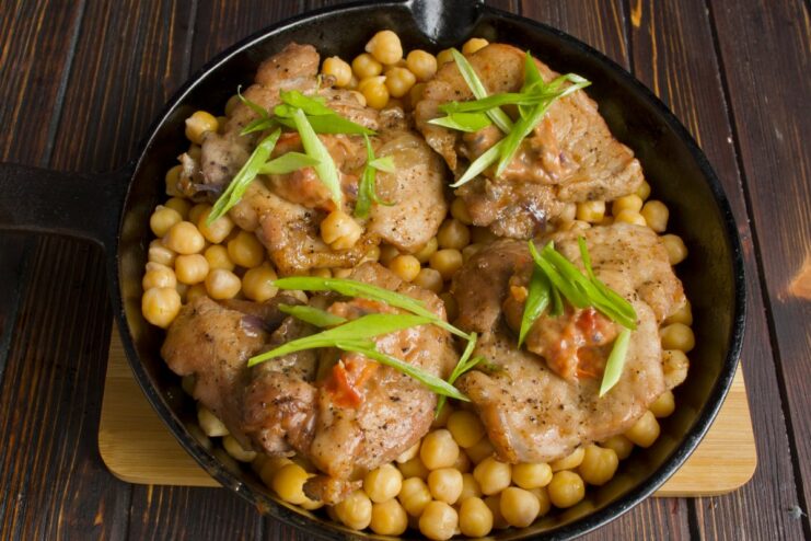 Combining all components and giving them a final bake to meld the flavors A skillet with chickpeas, topped with baked pork and sauce, ready for the final bake.