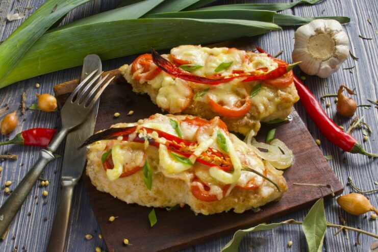 A plate of delicious oven-baked chicken fillet with melted cheese and fresh herbs.
