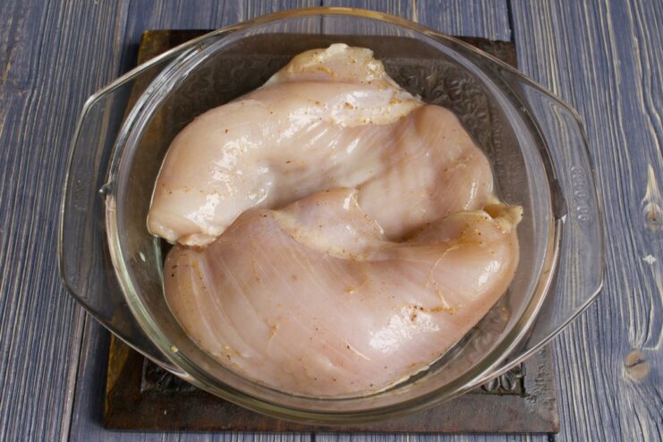 Placing raw chicken fillets into a bowl with marinade.