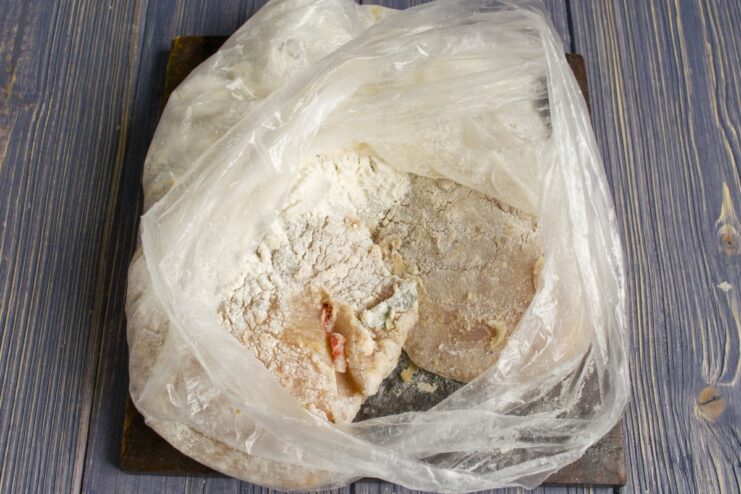 Coating a marinated chicken fillet in a bag with flour and salt.
