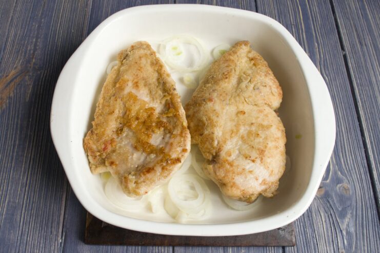 Placing pan-seared chicken fillets over a layer of onions in a baking dish.