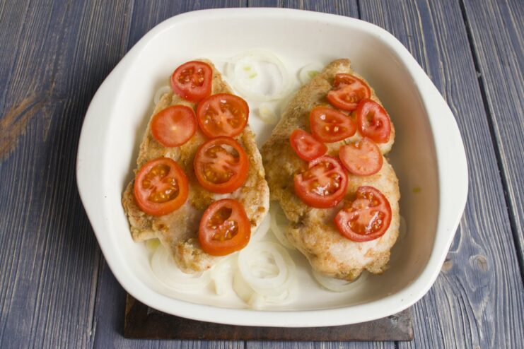 Adding sliced cherry tomatoes on top of the chicken fillets in the baking dish.