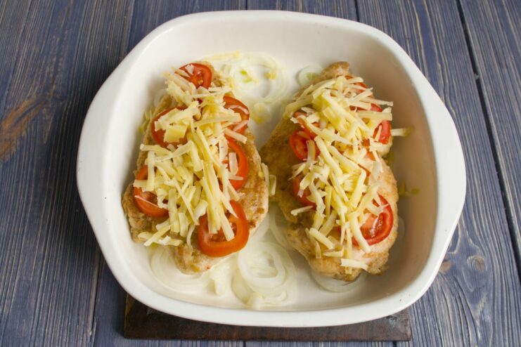 Sprinkling a thick layer of grated cheese over the tomatoes and chicken.