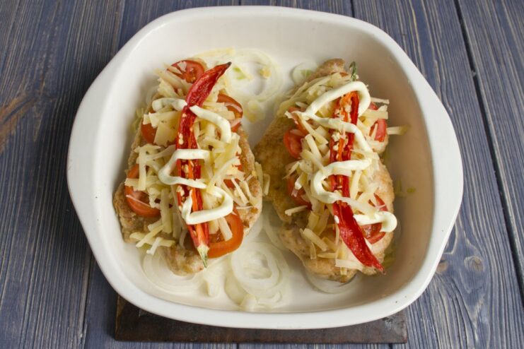 Chicken fillets topped with cheese, chili, and mayonnaise, ready to be baked.