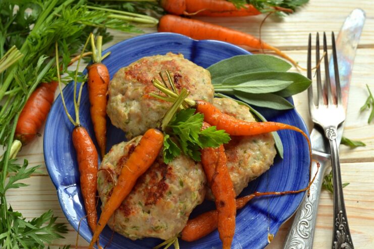 A plate of baked meat patties with rolled oats and vegetables, served with carrots and fresh herbs.
