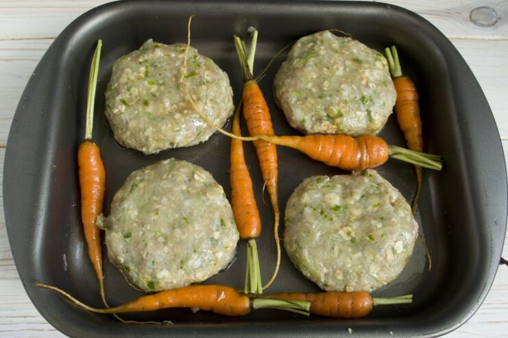 Shaping the Patties and Arranging on a Baking Sheet Raw meat patties and baby carrots arranged on a baking dish, ready for the oven.