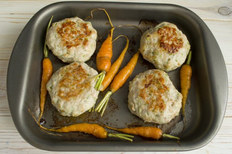 Baking the Patties Until Golden Brown Meat patties and carrots baking in the oven, being flipped to ensure even cooking.