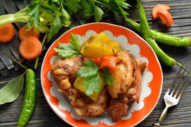A serving of oven-baked chicken with potatoes in a white bowl, garnished with fresh herbs.