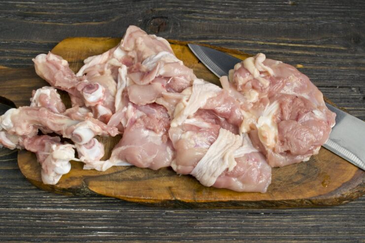 How to Debone Chicken Thighs for Faster Cooking A pair of hands deboning a raw chicken thigh on a cutting board.