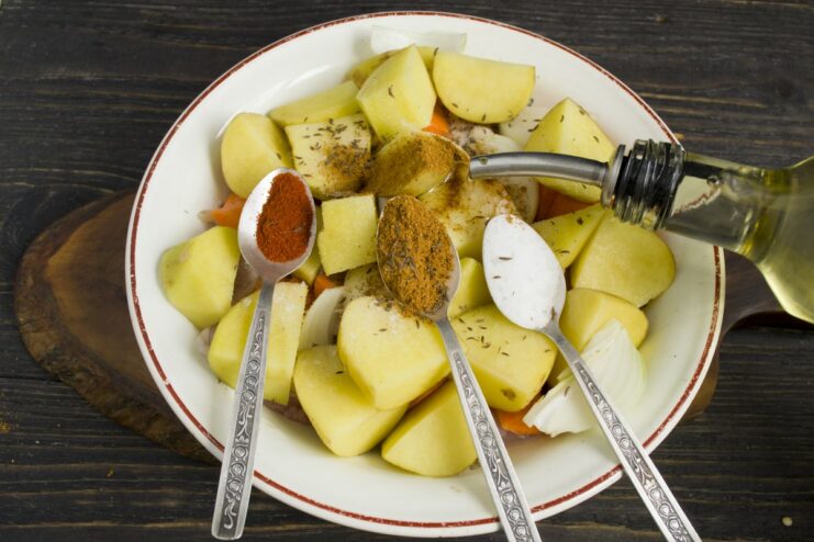 Seasoning the Chicken and Vegetables Before Baking A hand mixing chicken, potatoes, and vegetables with spices and oil in a large bowl.