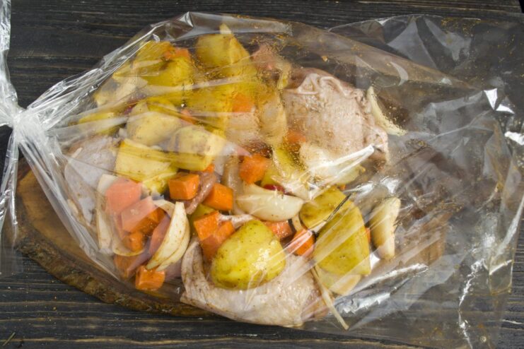 Using a Roasting Bag for Juicy Chicken and Veggies Seasoned chicken and vegetables being transferred from a bowl into a clear roasting bag.