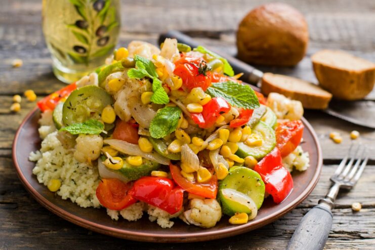 A white bowl filled with Moroccan-style roasted vegetables and couscous, garnished with fresh mint.