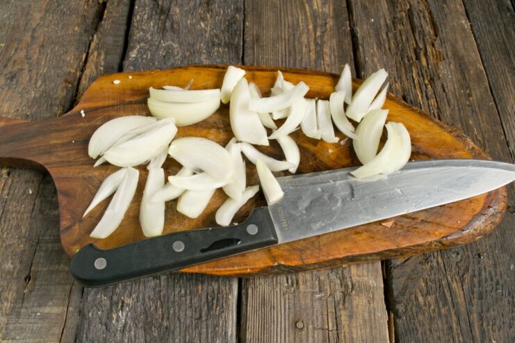 Cutting the onion into thick wedges prevents it from burning during roasting. A hand chopping a white onion into large, coarse wedges on a wooden cutting board.