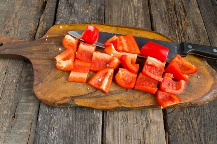 Preparing the bell pepper for even roasting. A red bell pepper being cut into large, uniform squares on a cutting board.