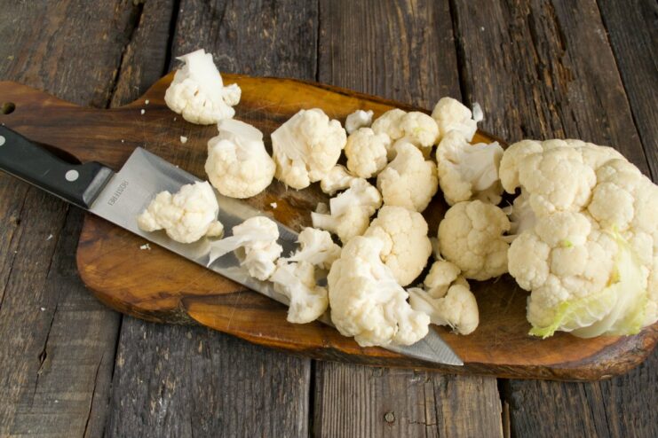 Separating cauliflower into bite-sized florets for the vegetable mix. A head of cauliflower being broken into smaller florets by hand.