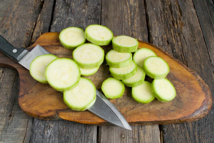 Slicing zucchini into thick rounds for roasting. A zucchini being sliced into thick, round pieces on a cutting board.