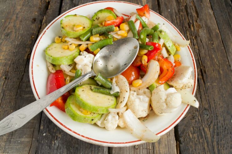 Combining all vegetables and seasonings before roasting. A large bowl of mixed chopped vegetables being seasoned with herbs, spices, and oil.