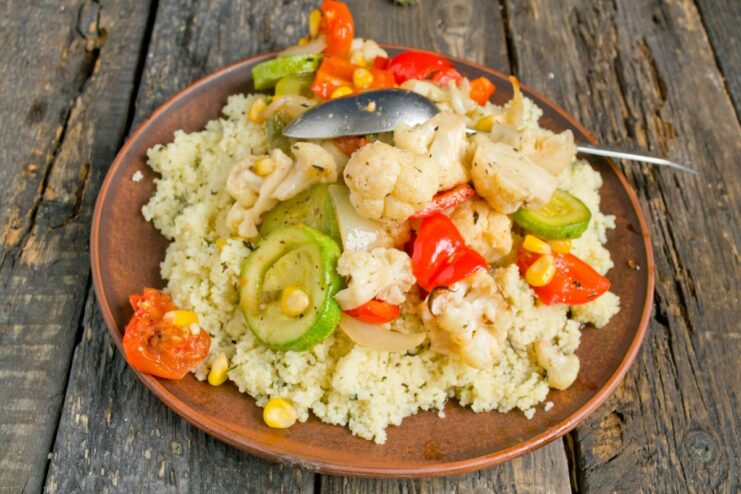 Assembling the final dish: a bed of couscous topped with roasted vegetables. A serving of fluffy couscous on a plate, with roasted vegetables being spooned on top.