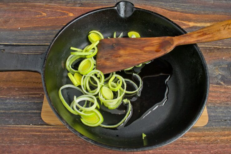 Start by sautéing sliced leeks in olive oil until softened. Sliced leeks being added to olive oil in a hot frying pan.
