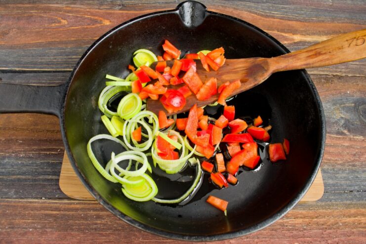 Add chopped bell pepper to the leeks for extra flavor and color. Chopped red bell pepper being added to the leeks in the frying pan.