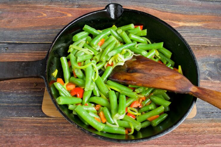 Cook the vegetables over medium heat until tender. Green beans added to the pan with leeks and peppers, being sautéed.