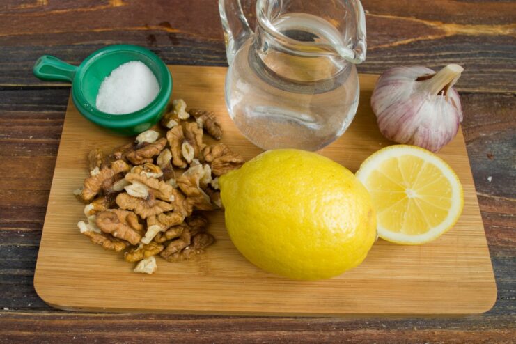 Gather walnuts, garlic, and lemon to make the traditional Georgian bazhe sauce. Ingredients for the bazhe sauce: walnuts, garlic, and a lemon on a wooden board.