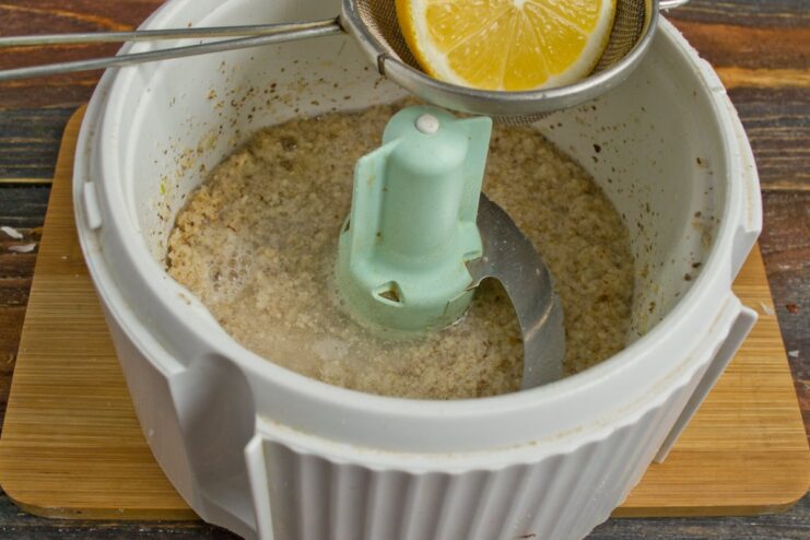 Combine ground walnuts and garlic with water and lemon juice for the sauce base. A blender bowl with ground walnuts, garlic, water, and lemon juice, ready for blending.