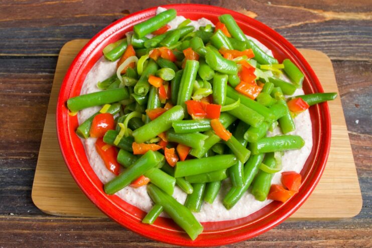 Serve the warm sautéed vegetables over the cool, creamy bazhe sauce. Sautéed green beans, leeks, and peppers being placed on top of the bazhe sauce.
