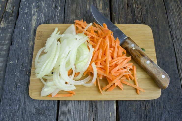 Sautéing onions and carrots to build the flavor base Finely chopped onions and julienned carrots being sautéed in a pan.