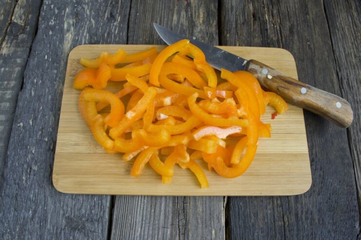 Adding colorful bell peppers to the sautéed vegetables Thin strips of red bell pepper being added to the pan with onions and carrots.