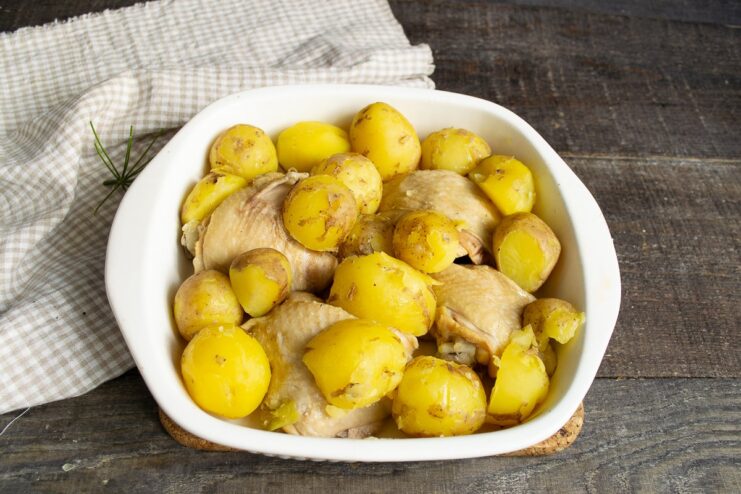 Adding Par-Boiled Potatoes to the Chicken Par-boiled new potatoes being added to the baking dish with chicken pieces.