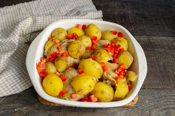 Adding Diced Bell Pepper for Flavor and Color Cooked chicken and potatoes in a baking dish being sprinkled with diced red bell pepper.
