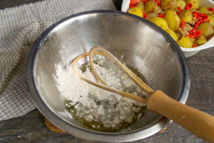 Whisking Flour into Broth to Create a Sauce Base A hand whisking flour into chicken broth in a white bowl to make a smooth sauce base.