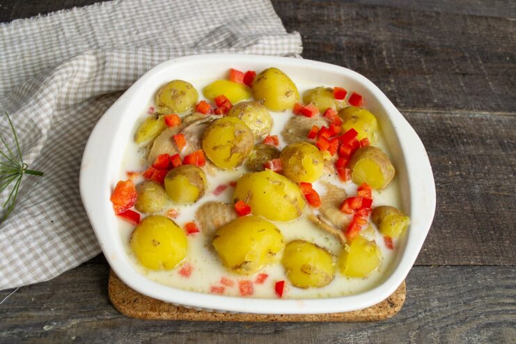 Pouring the Creamy Sauce Over Chicken and Potatoes The prepared white sauce being poured over chicken and potatoes in a baking dish.