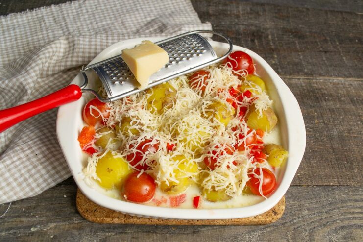 Topping with Grated Cheese for a Golden Crust Grated hard cheese being sprinkled over the chicken, potatoes, and sauce in the baking dish.