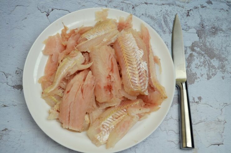 Raw pollock fillets being separated from the skin and bones on a cutting board.