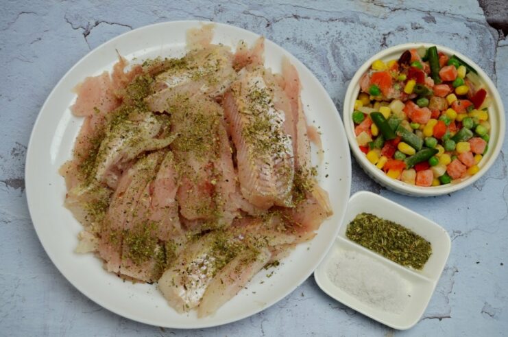 Pieces of raw pollock fillet in a bowl being seasoned with salt and Italian herbs.
