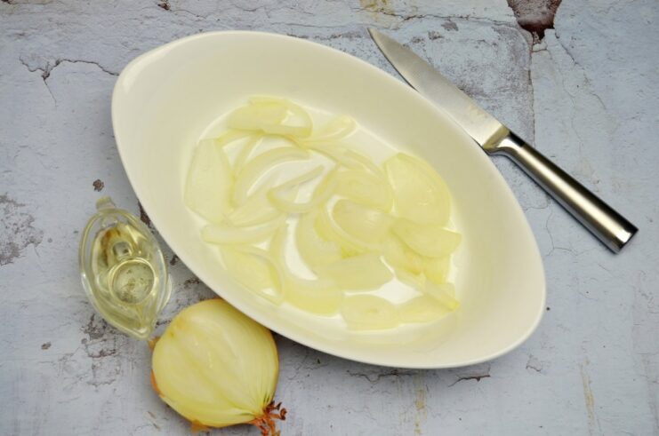 Sliced raw onions layered at the bottom of a ceramic baking dish.