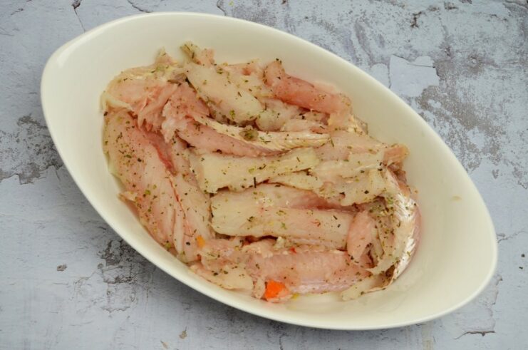 Seasoned pollock fillets being layered over vegetables in a baking dish.