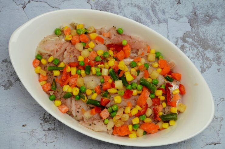 A final layer of frozen mixed vegetables spread over the pollock fillets in the baking dish.