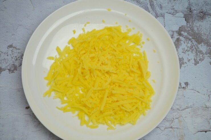 A block of hard cheese being grated on a coarse box grater.