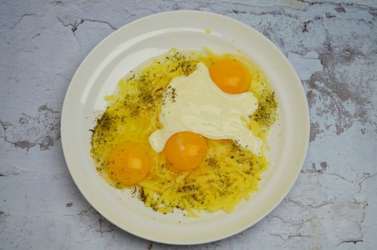 A bowl with eggs, cheese, smetana, and herbs being mixed for the casserole sauce.