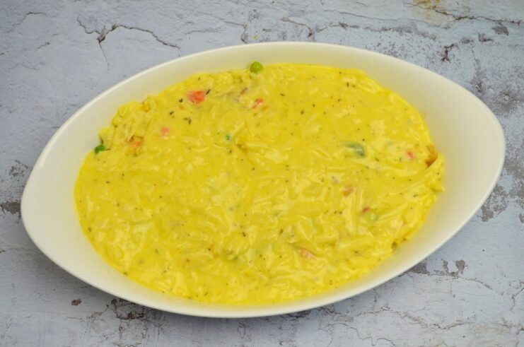 The fish and vegetable casserole being covered with a creamy egg and cheese sauce.