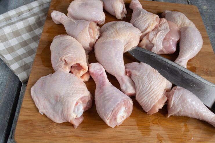 Preparing the Chicken Legs for Frying Raw chicken legs being cut at the joint on a cutting board.