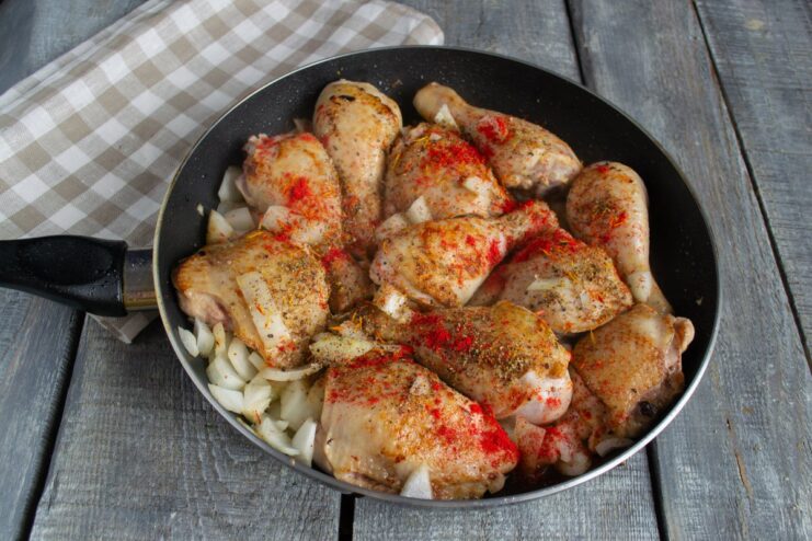 Seasoning the Chicken with a Fragrant Spice Mix A hand sprinkling a ground spice mix over chicken and onions in a pan.
