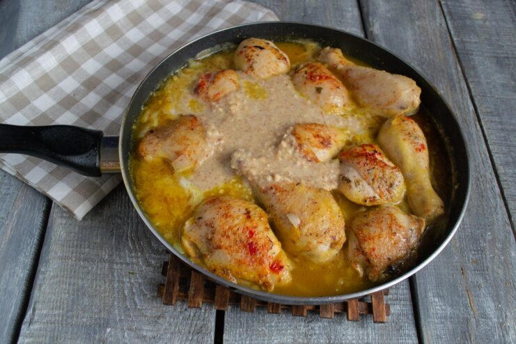 Combining the Chicken with the Nut Sauce and Simmering Creamy nut purée being stirred into the pan with the fried chicken pieces.