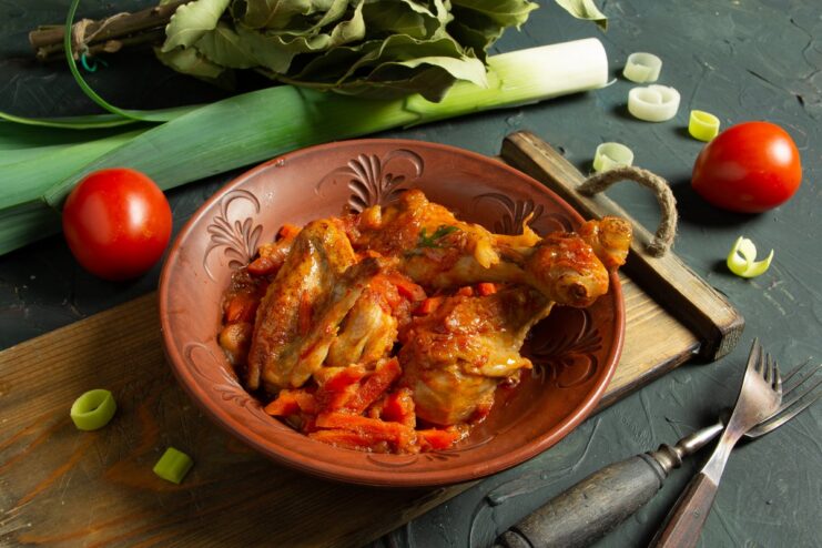 A bowl of aromatic Georgian Chakhokhbili, a chicken stew with tomato paste, garnished with fresh herbs.